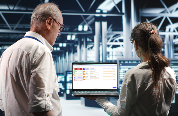 Two professionals reviewing real-time data analytics on a laptop in a high-tech industrial environment.