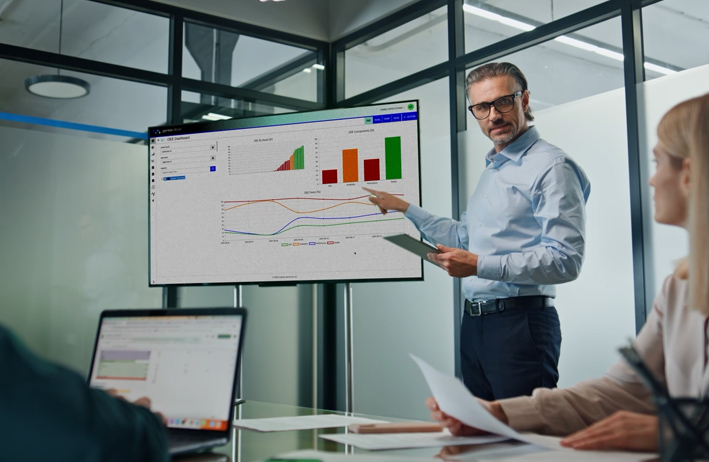 A business professional presenting data insights on a large screen to colleagues in a modern office setting.