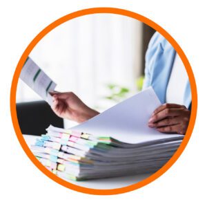 Person reviewing large stacks of paperwork and documents related to compliance or quality management.